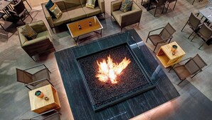 Un área de estar moderna con una chimenea central, diversas opciones de asientos, incluyendo sofás y sillones, y una variedad de mesas.