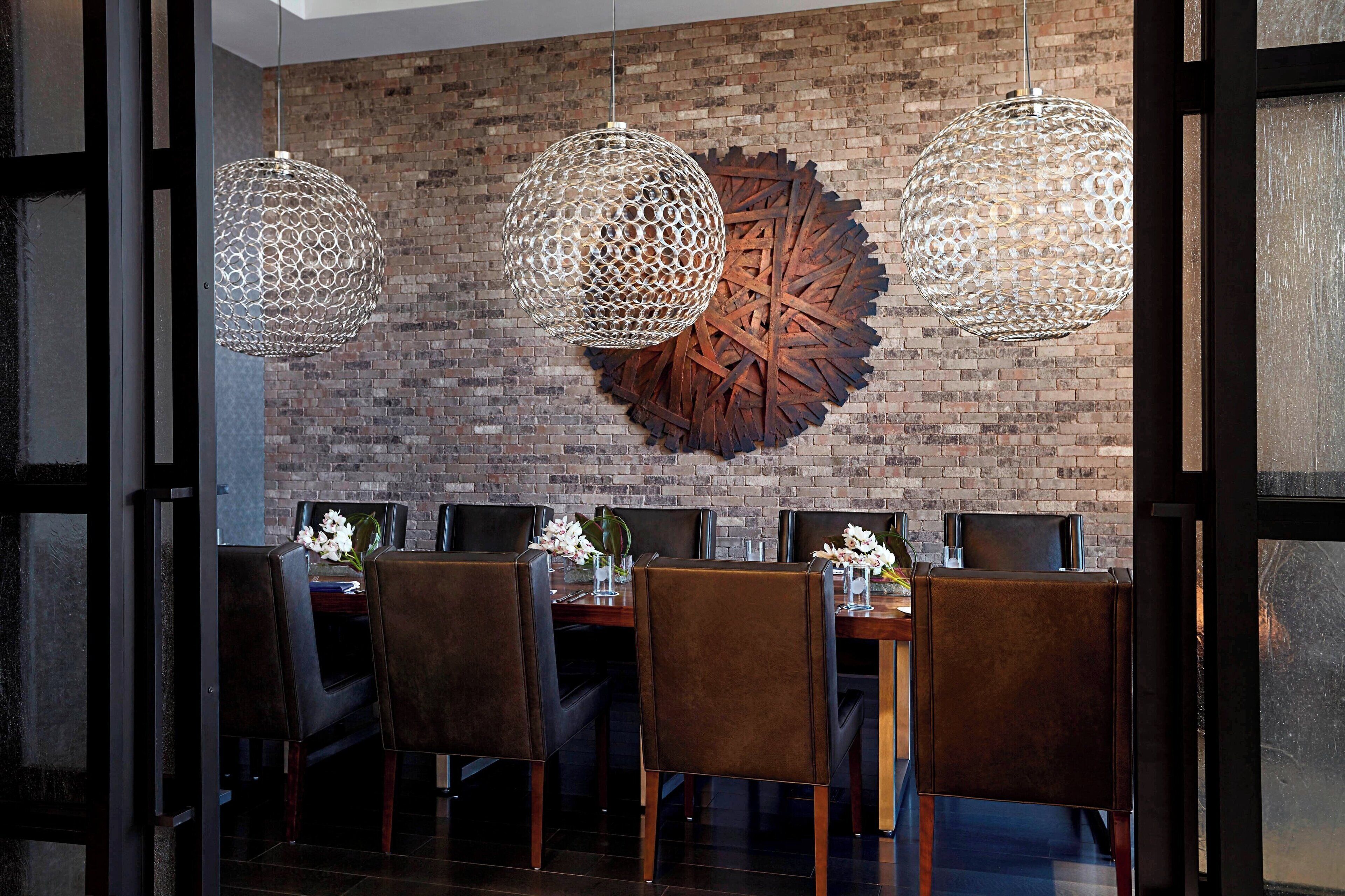 A dining area with a brick wall, three hanging spherical light fixtures, and a large decorative metal piece.