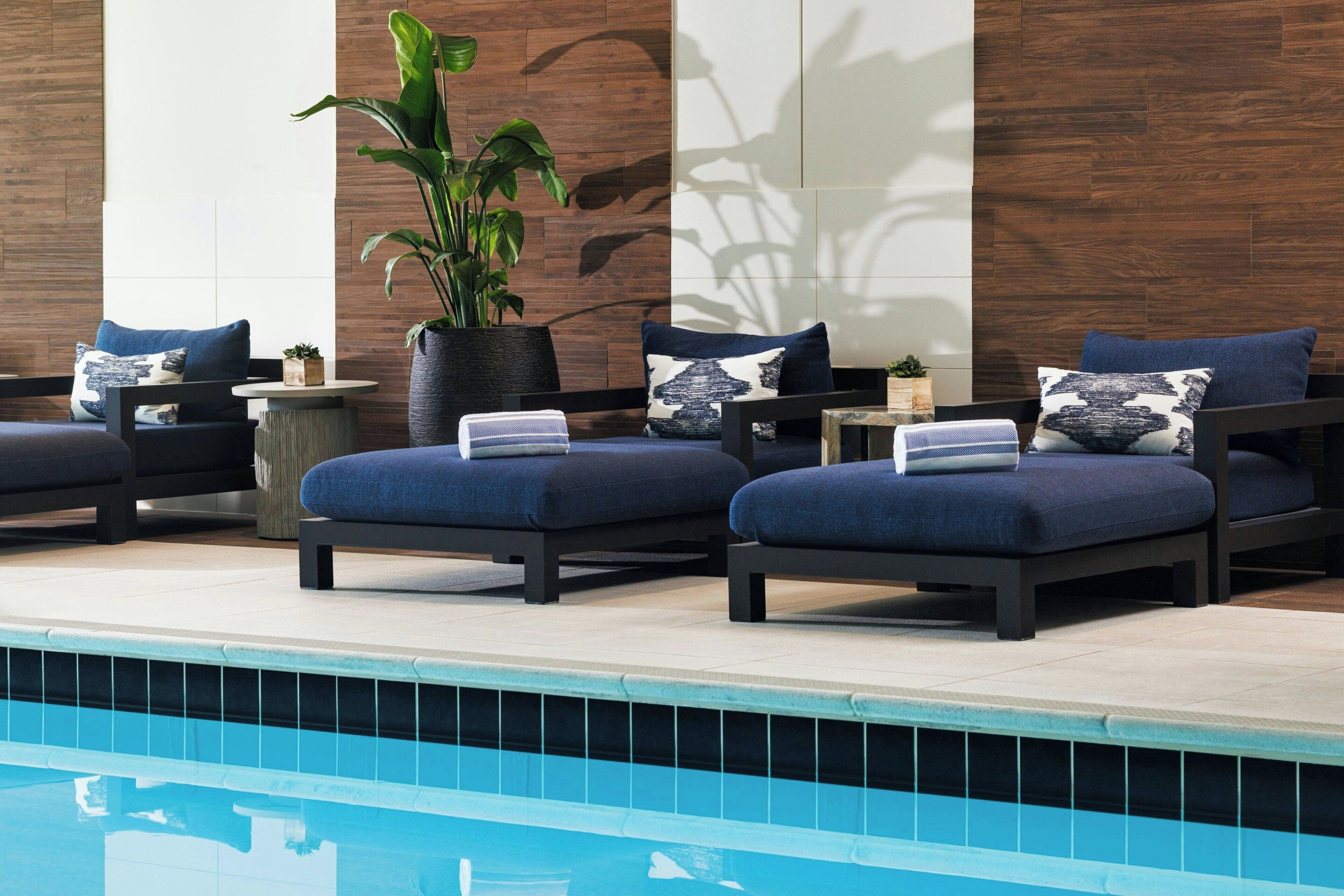 A poolside lounge area with dark-colored lounge chairs, a potted plant, and a tiled pool.
