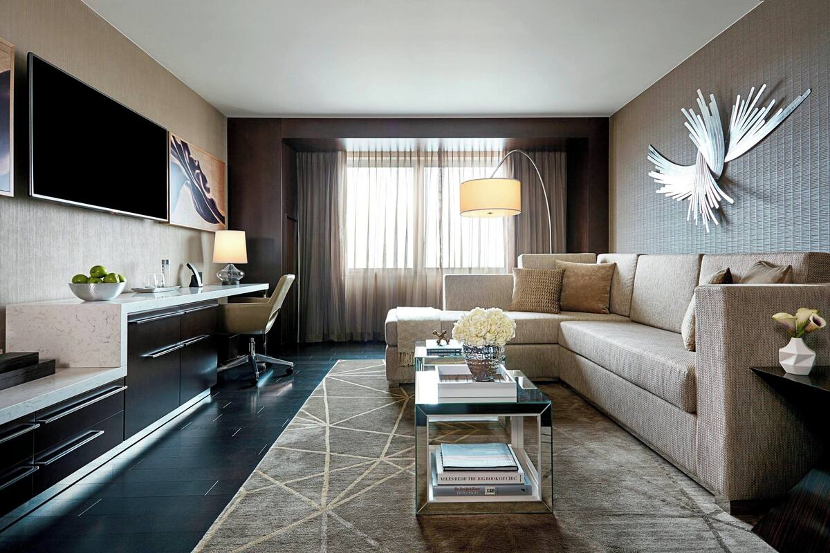 Ein modernes Hotelzimmer mit Flachbildfernseher, einer Couch, einem Couchtisch und einer Essecke mit Stuhl und Lampe.