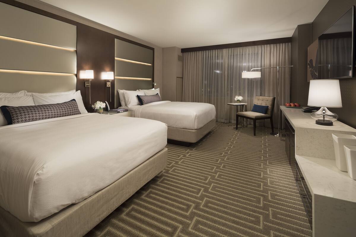 Ein Hotelzimmer mit zwei Betten, einem Schreibtisch, einem Stuhl und einem kleinen Tisch mit einer Lampe.