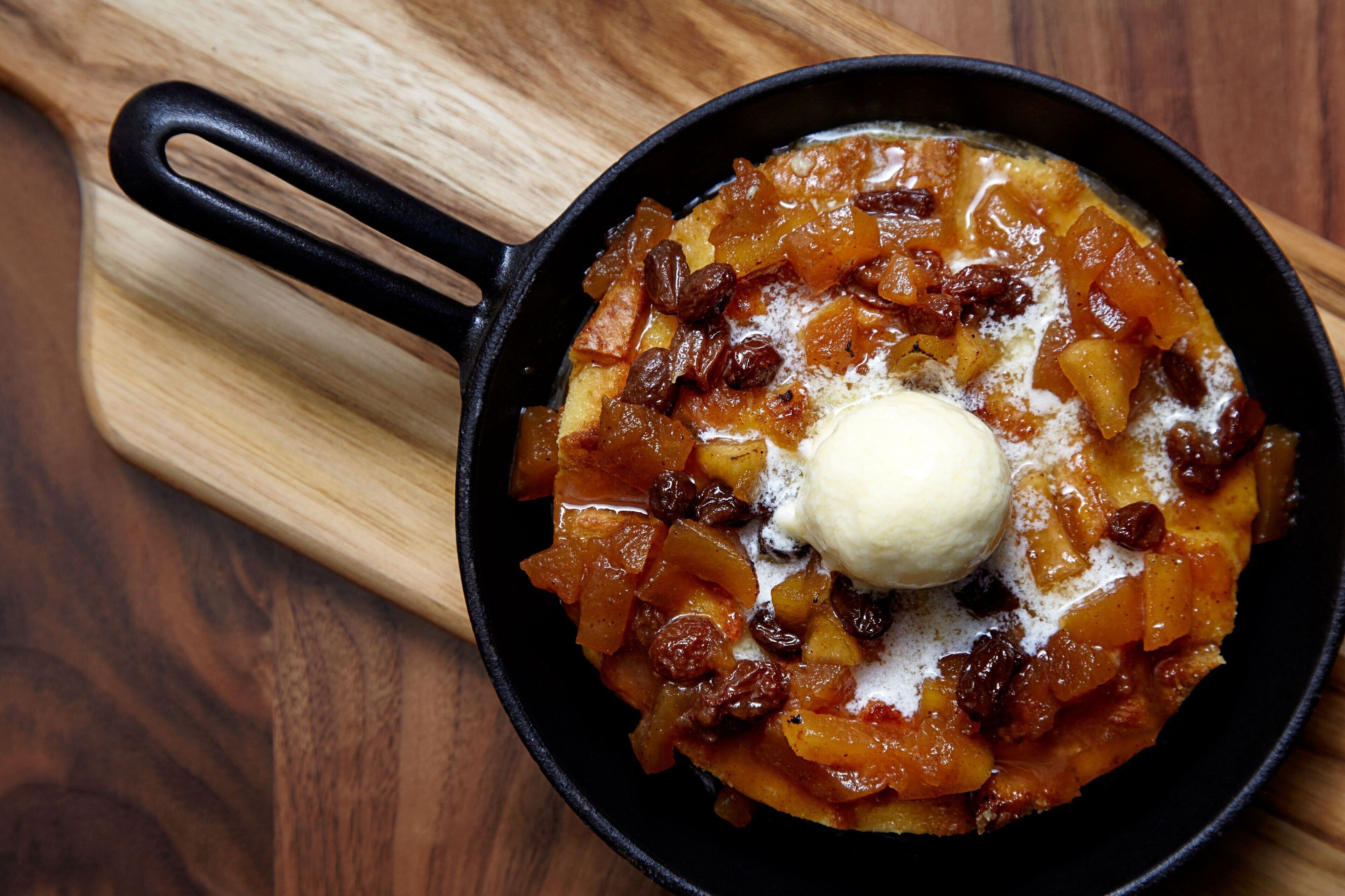 A skillet with a dessert, possibly apple crisp, on a wooden board.