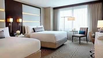 A hotel room with two beds, a desk, a chair, and a large window with curtains.