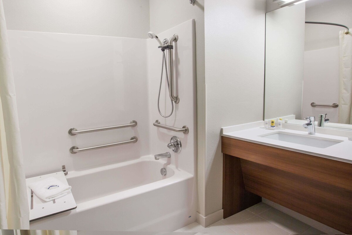 Un baño con una bañera blanca, un tocador de madera, un espejo y un perchero para toallas.