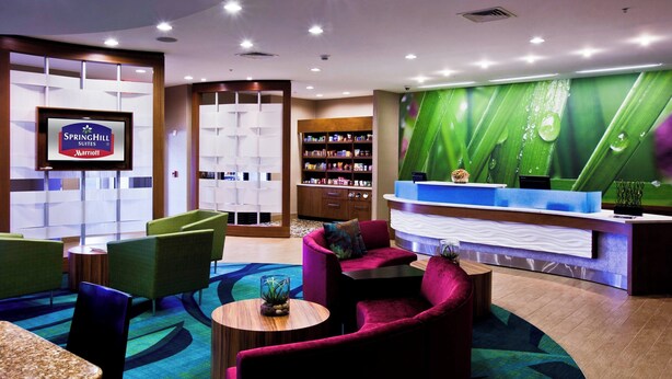 A hotel reception area with a reception desk, seating area, and a large screen displaying the hotel name. - Springhill Suites Mobile (Mobile)