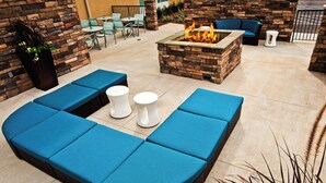 A stone fireplace with a fire, blue cushioned seating, and a small table with white stools. - Springhill Suites Mobile (Mobile)