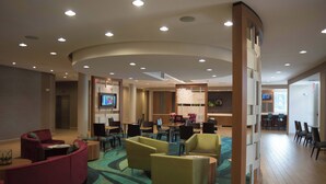 A modern hotel lobby with a curved ceiling, multiple seating areas, a television, and a dining area. - Springhill Suites Mobile (Mobile)