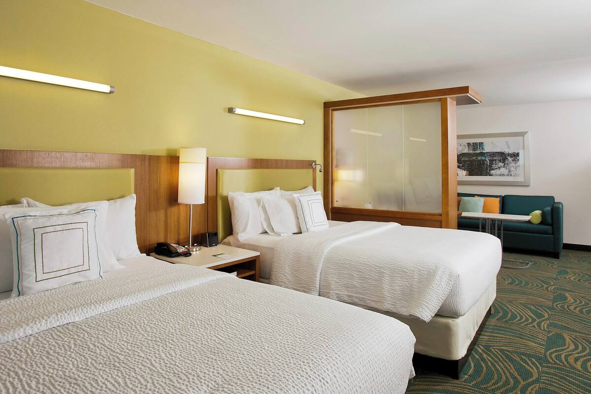 A hotel room with two beds, a desk, a chair, a sofa, and a large window.
