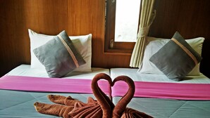 Habitación de hotel con una cama que incluye dos almohadas, una colcha rosa y dos toallas dispuestas en forma de corazón.