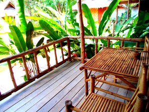 A wooden deck with a bamboo railing, surrounded by lush green foliage.