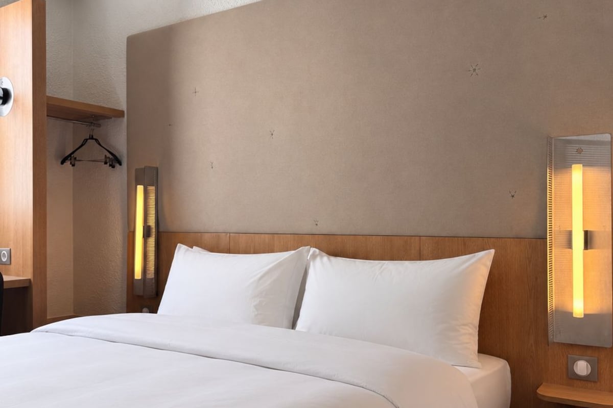 A hotel room with a large bed, a wooden headboard, bedside lamps, and a hanging coat rack.