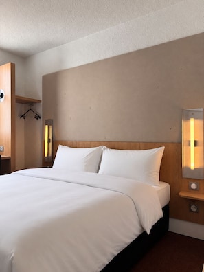 A hotel room with a large bed, a wooden headboard, bedside lamps, and a hanging coat rack.