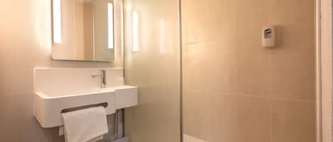 A modern bathroom with a white sink, mirror, and glass shower enclosure.