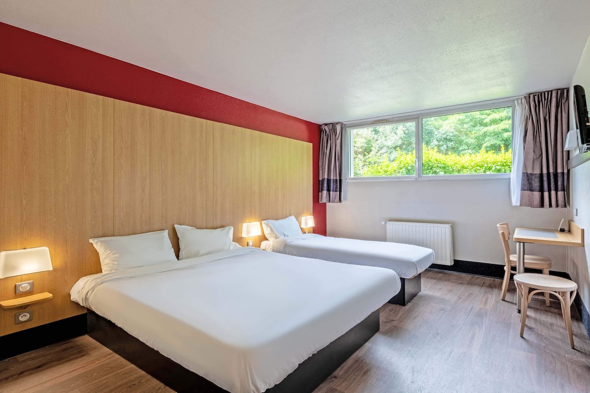 Quarto de hotel com duas camas, uma escrivaninha, uma cadeira e uma janela com cortinas.