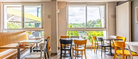 Un café moderne doté d’un espace salon confortable, de grandes fenêtres et offrant une vue sur la verdure.