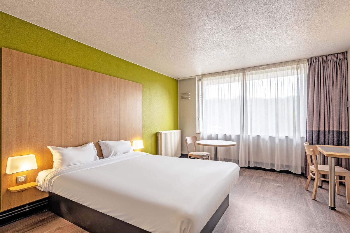 Quarto de hotel com uma cama grande, uma mesa redonda e uma cadeira.