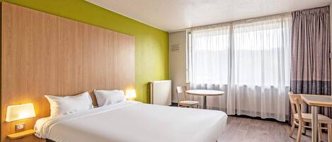 A hotel room with a large bed, a round table, and a chair.