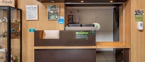 A reception desk with a wooden counter, a glass display case with bottles, and a sign indicating a restaurant.