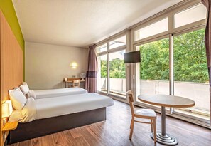 Een hotelkamer met een bed, een tafeltje, een stoel, een televisie en grote ramen.