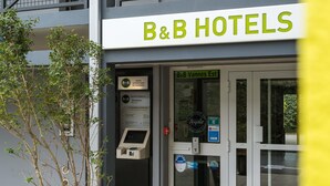 Entrada de un hotel B&B con una recepción, un cartel que indica 'B&B Vannes Est' y un pequeño árbol en la parte delantera.