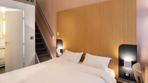 Habitación de hotel con cama, cabecera de madera, dos lámparas de noche, una silla y una escalera.