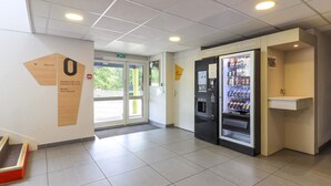 A hotel lobby with a vending machine, a reception desk, and a door leading outside. - B&B HOTEL Chalon-sur-Saône Sud (Saint-Remy)