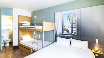 Une chambre d’hôtel avec un lit superposé, un lit simple, une salle de bain avec des toilettes et un lavabo, et un téléviseur fixé au mur.