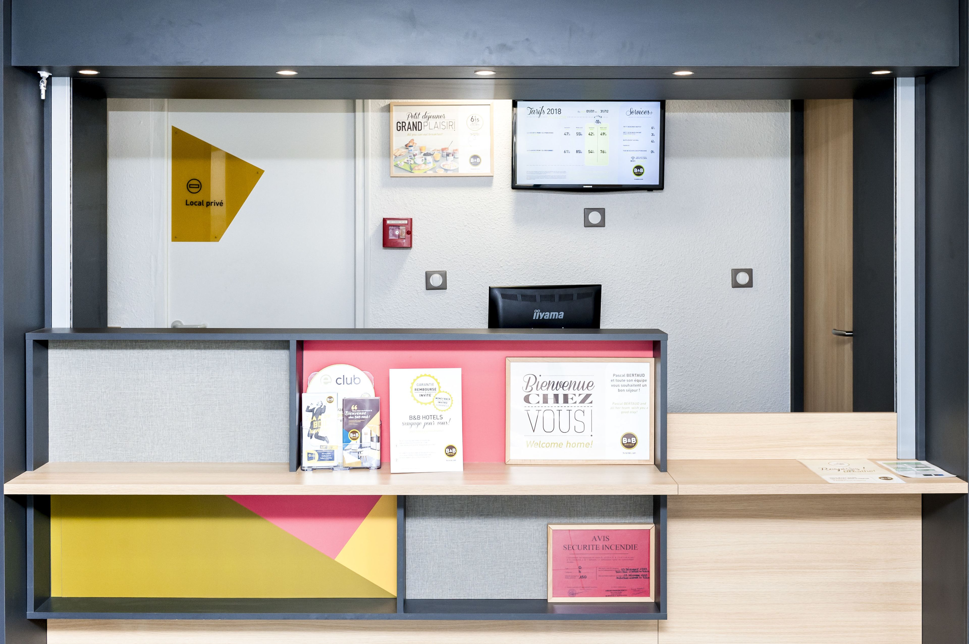 Een receptiebalie met diverse informatieposters, een digitaal scherm en een bordje met 'Local privé'.