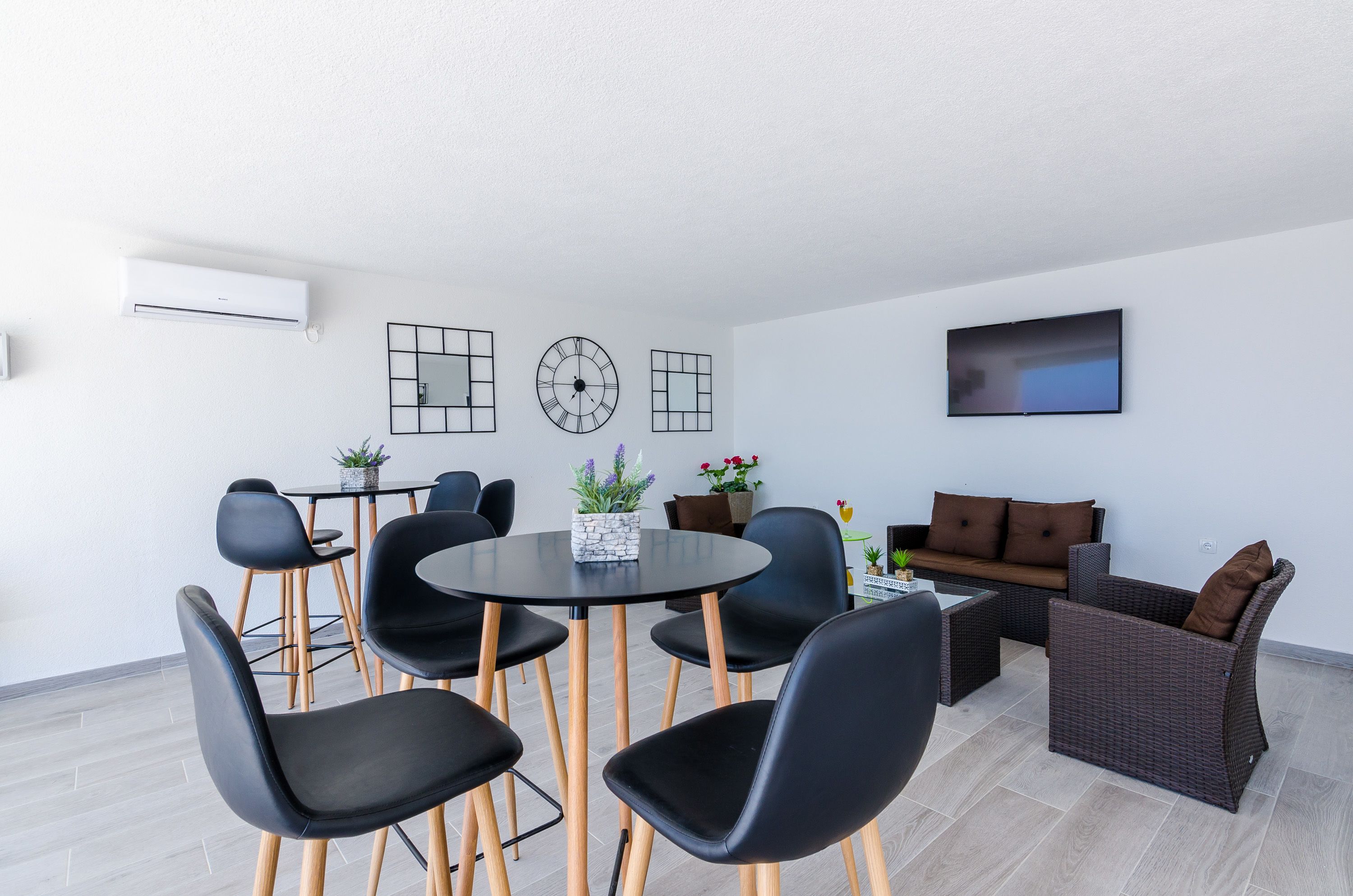 Un salon moderne avec une table ronde, des chaises noires, un canapé et un téléviseur à écran plat fixé au mur.