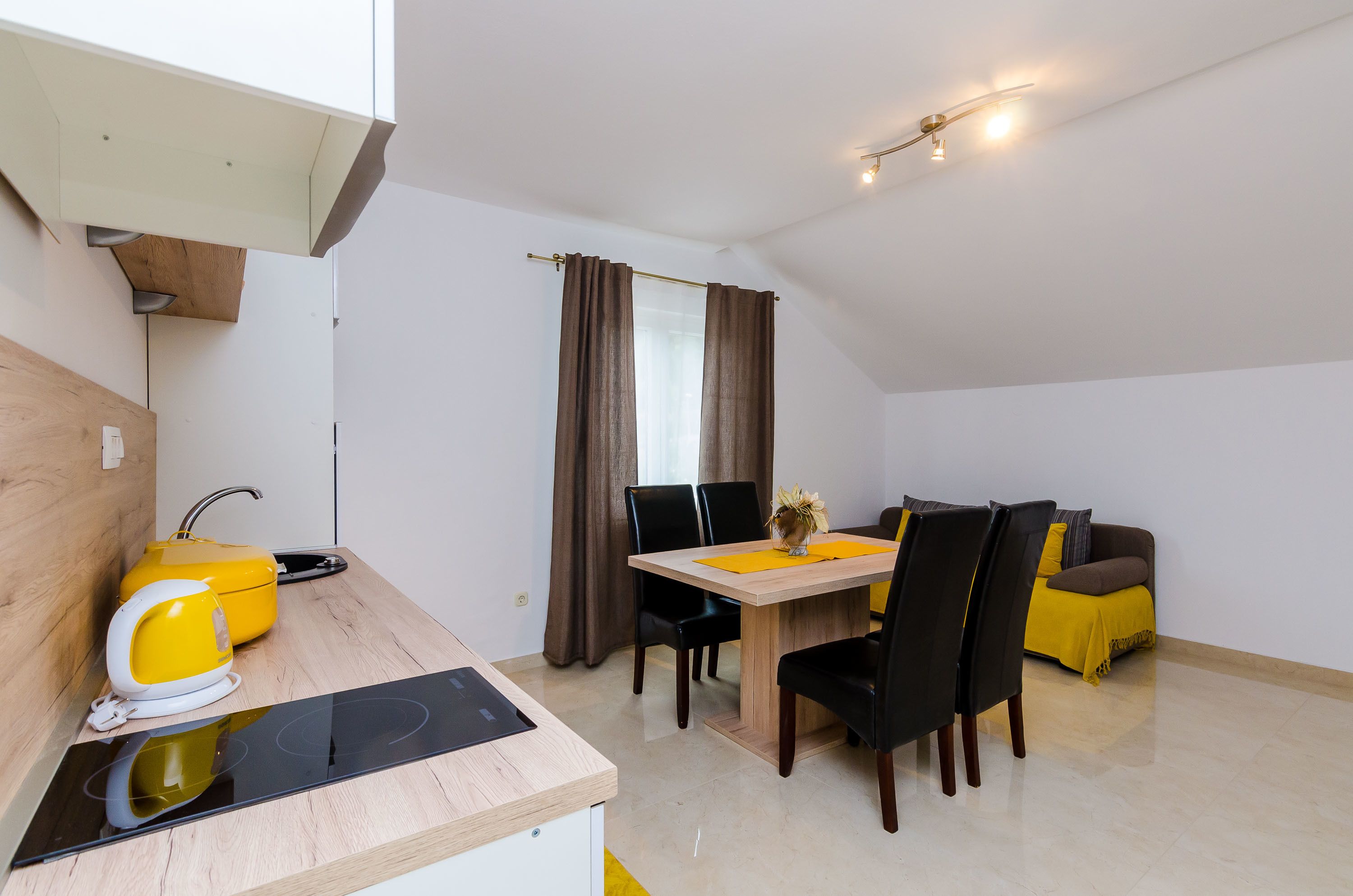 Una cocina moderna con estufa integrada, un hervidor amarillo y un comedor con mesa de madera y sillas negras.