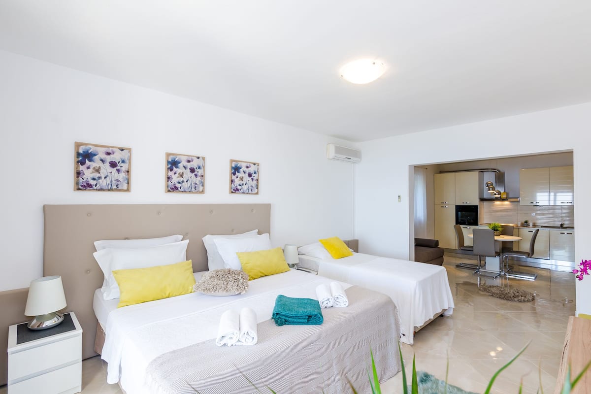 Hotellihuoneessa on kaksi sänkyä, pieni työpöytä, tuoli ja taustalla näkyy pieni keittiönurkkaus.