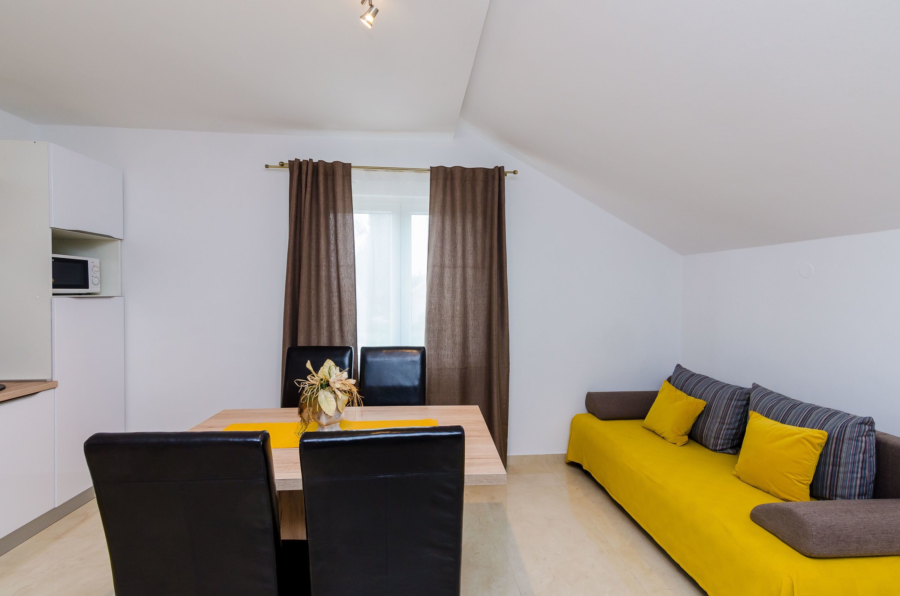 A modern living room with a yellow sofa, black chairs, a wooden table, and a TV on a shelf.