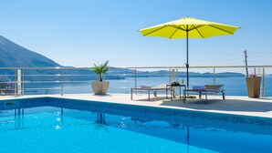 Una piscina amb vistes a un llac i muntanyes, envoltada de gandules i un parasol groc.