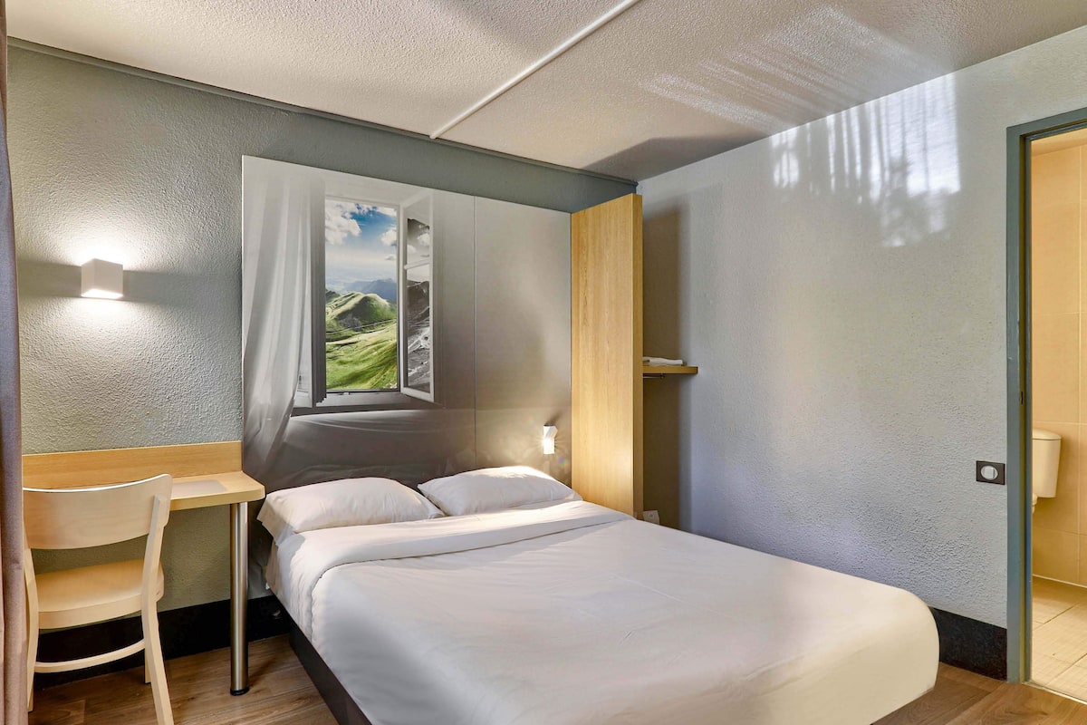 Ein Hotelzimmer mit Bett, Schreibtisch und Fenster mit Blick auf grüne Hügel.
