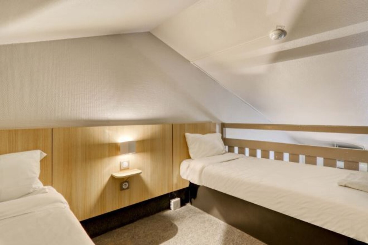 A small, cozy bedroom with two beds, a nightstand, and a ceiling light.