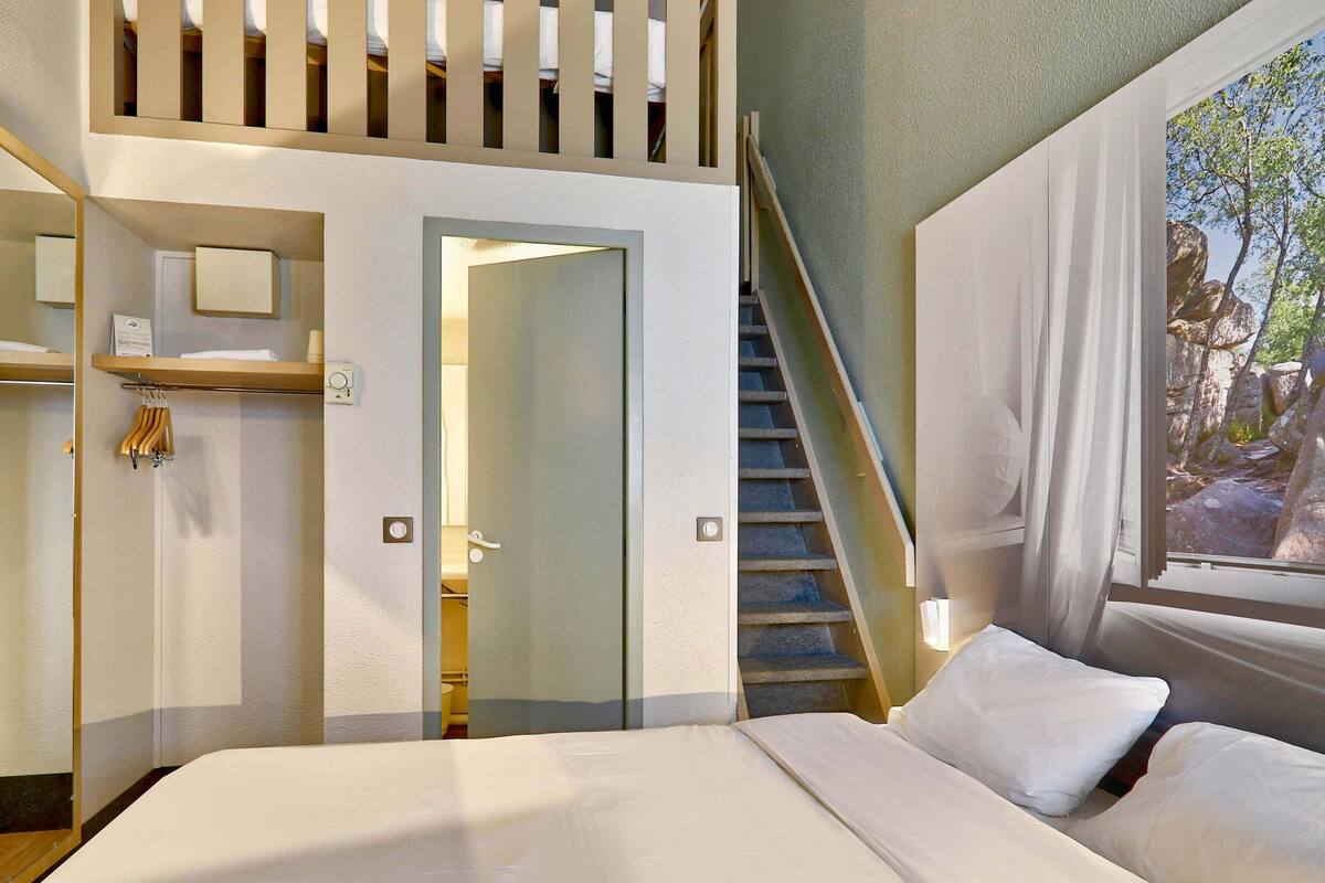 Ein Hotelzimmer mit Bett, Treppe, Spiegel und Fenster mit Blick auf Bäume.