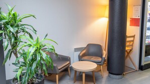 Un vestíbulo moderno con una planta en maceta, dos sillones de cuero, una mesa redonda de madera y un pilar grande.
