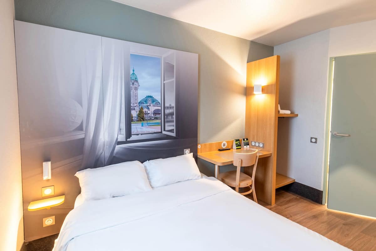 A hotel room with a large bed, a desk, and a wall-mounted TV.