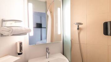 Un baño con lavamanos blanco, un espejo, toallero, cabezal de ducha manual y panel de control en la pared.