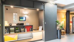 Un mostrador de recepción con una pantalla digital, carteles informativos y una planta en maceta.
