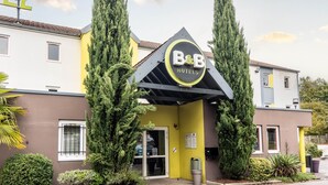 Un hotel B&B con fachada amarilla, dos cipreses altos y un letrero sobre la entrada.