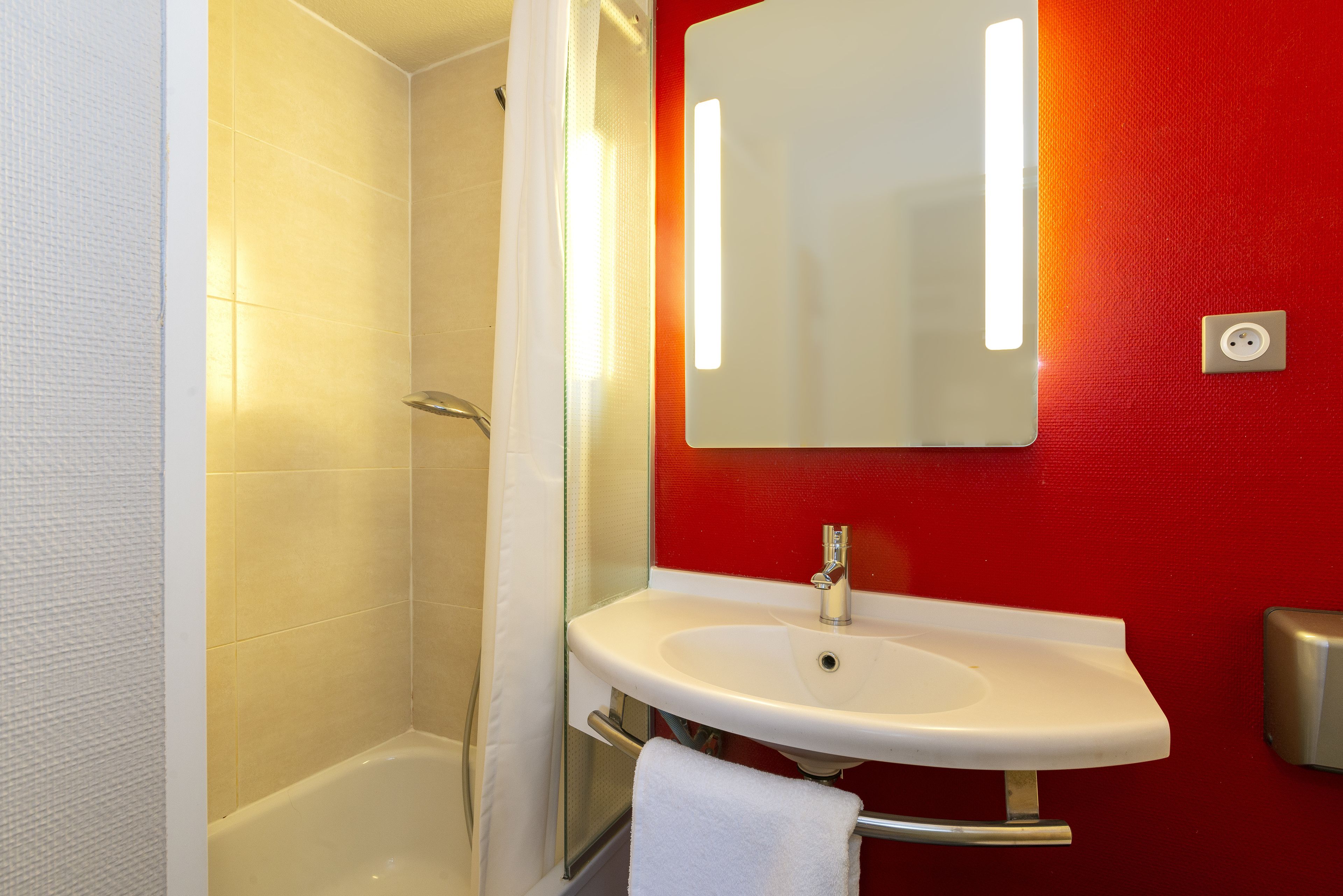 A bathroom with a white bathtub, a white sink with a mirror above it, and a red wall.