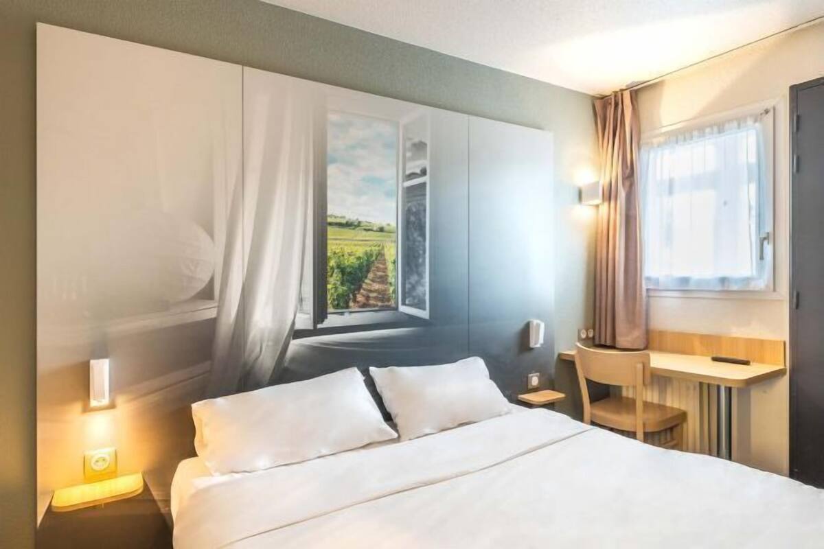Une chambre d’hôtel avec un lit, un bureau et une vue sur la campagne, visible par la fenêtre.