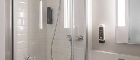 Une salle de bain moderne dotée d’une douche à parois de verre, d’un pommeau de douche à main, d’un porte-serviettes et d’un distributeur de savon.