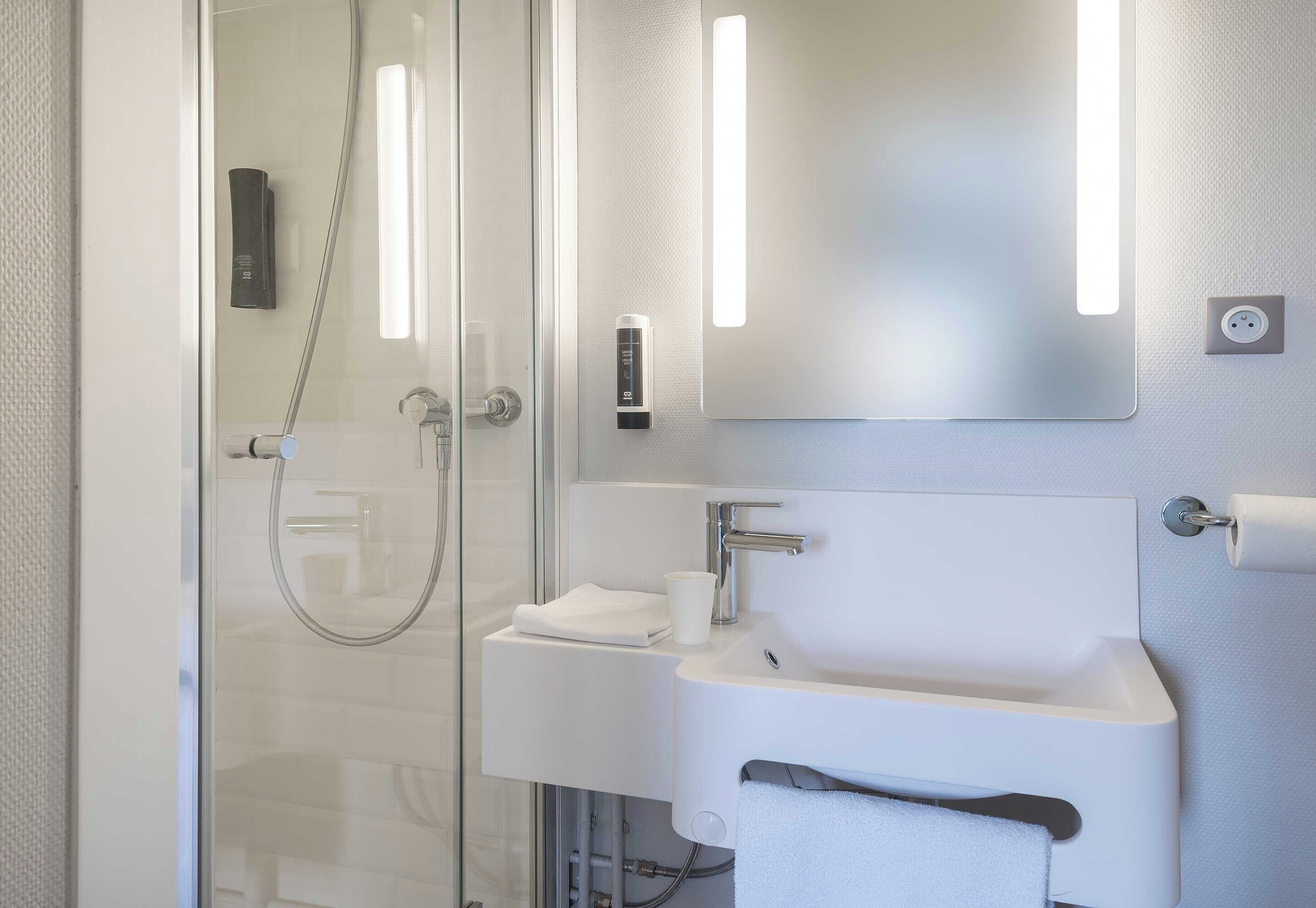 A modern bathroom with a glass shower enclosure, a white sink, and a mirror with integrated lighting.