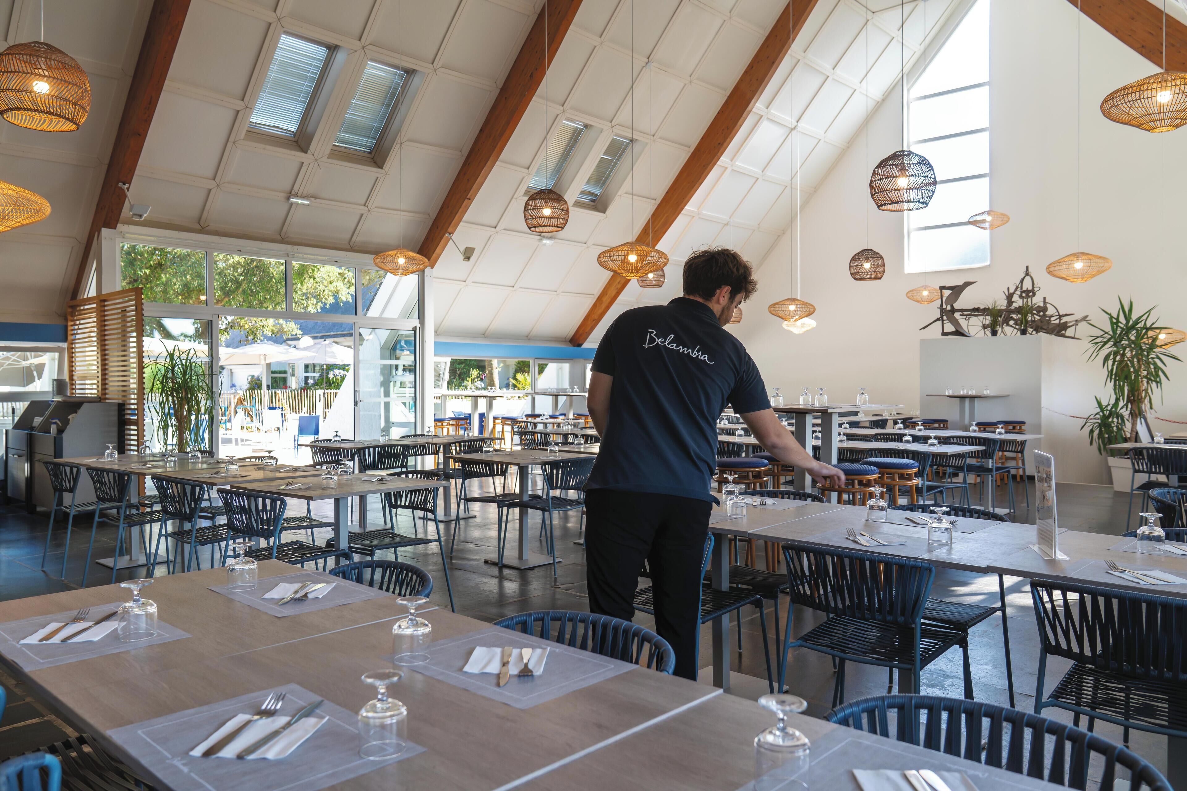 A spacious restaurant with high ceilings, natural light, and modern furnishings.