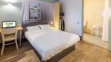 A hotel room with a bed, a desk with a laptop, a window with a view of a bridge, and a bathroom with a shower curtain.