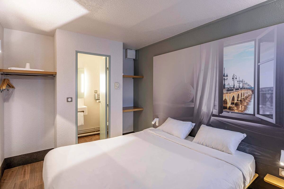 Quarto de hotel com uma cama grande, vista de uma ponte pela janela e uma porta para um banheiro.