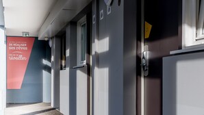 Un pasillo con puertas, un cartel rojo y una ventana.