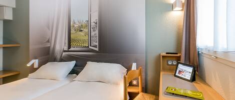 A hotel room with a bed, a desk with a tablet, a chair, and a large wall mural.